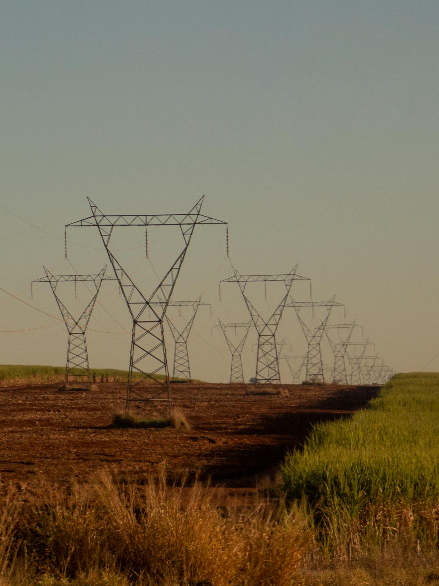 Power lines with wires located on ground near grassy field against cloudless sky in countryside in summer day in nature